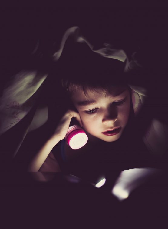 Boy with flashlight under blanket