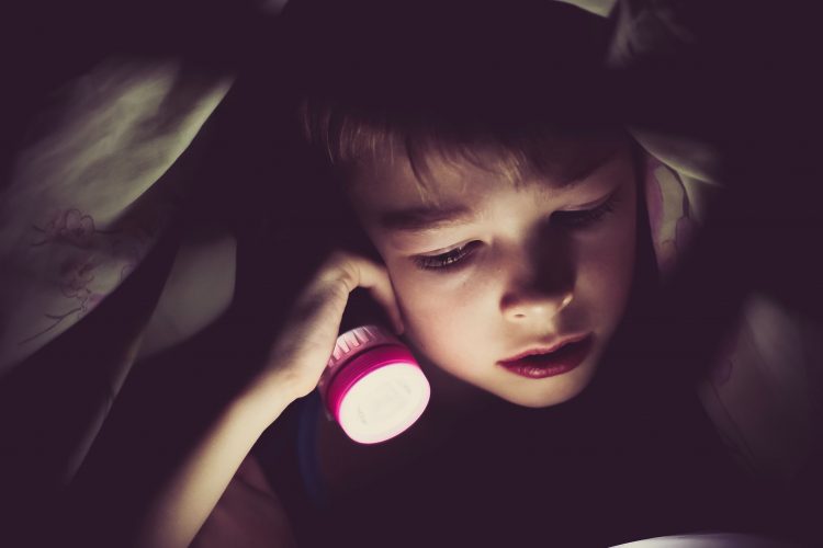 Boy with flashlight under blanket